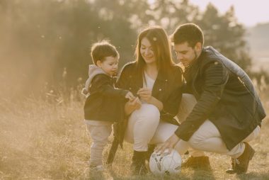 A cheerful family bonding outdoors with a soccer ball, enjoying a sunny day in the grass.
